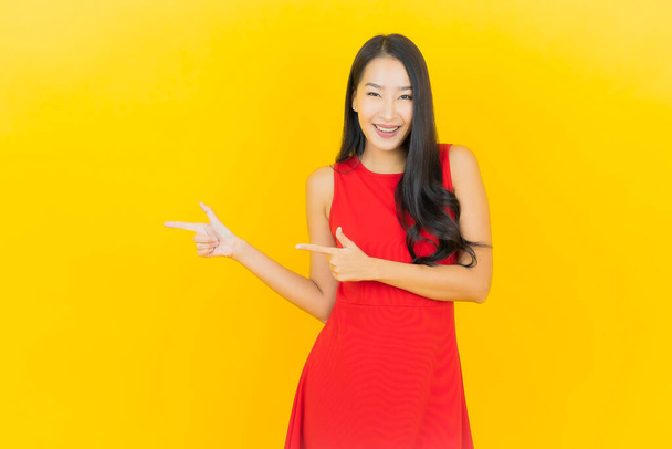 Портрет красивая молодая азиатская женщина носить красное платье улыбка с действием на желтый цвет фона - Фото, изображение