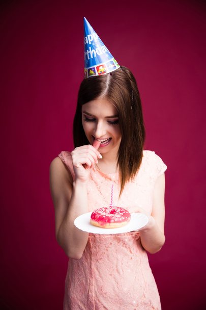 Pensive young woman holding donut with candle - 写真・画像