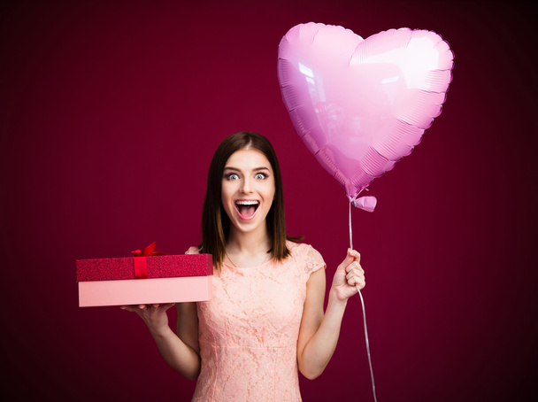 Surprised woman holding heart shaped balloon and gift box - Photo, Image