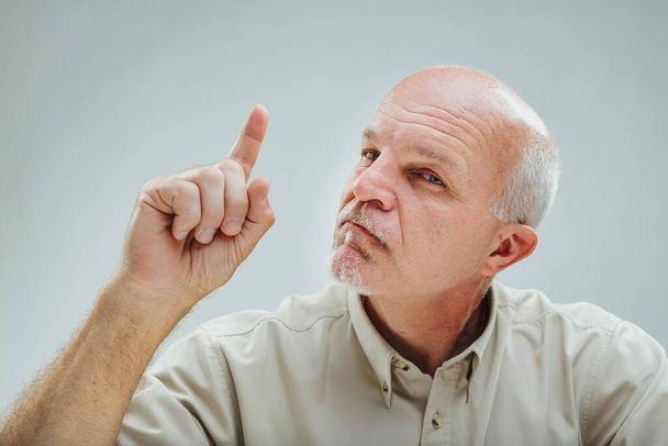 Зрелый человек испытывает момент осознания, поднимая указательный палец с вдумчивым выражением - Фото, изображение