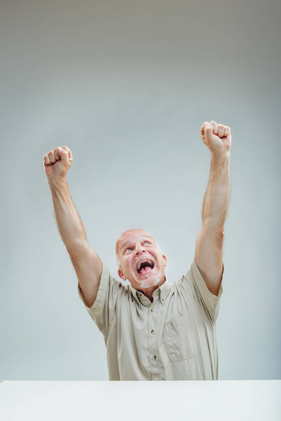 Радостный человек празднует с высоко поднятыми кулаками, с триумфом крича о невидимой победе - Фото, изображение