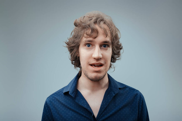 Hombre joven con una expresión intrigada y pelo rizado lleva una camisa de lunares azul marino, insinuando una personalidad juguetona - Foto, imagen