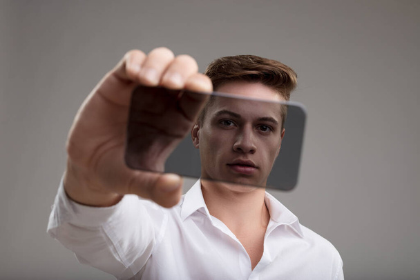 Чоловік у білій сорочці демонструє прозорий високотехнологічний смартфон, що символізує прозорість передових технологій - Фото, зображення
