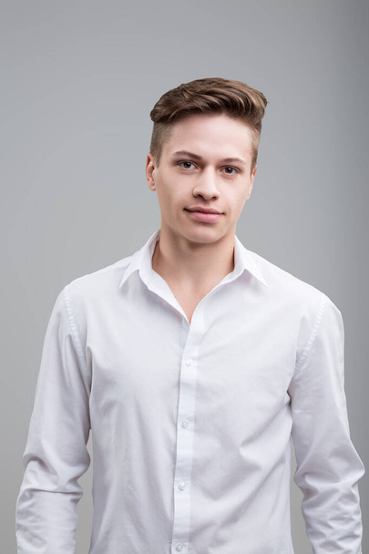 Selbstbewusster junger Mann in knackigem weißem Hemd, mit subtilem Lächeln und scharfem Blick, strahlt Nahbarkeit und Professionalität aus - Foto, Bild