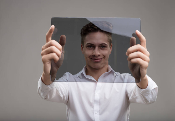 Muž v bílém pozvedne průhlednou futuristickou tabulku s tváří zarámovanou další vlnou inovací - Fotografie, Obrázek