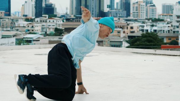 Profesjonalny biały B-boy tancerz ćwiczący taniec uliczny na dachu z miastem lub miastem. Motion shot młodego człowieka wykonującego taniec uliczny poprzez zamrożenie pozycji. Sport na świeżym powietrzu 2024. Endeavor. - Zdjęcie, obraz