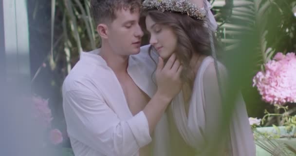 A young couple of lovers in light white robes on a swing among a blooming spring garden. Slow motion - Filmati, video