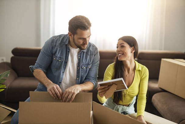 Glückliches junges Ehepaar zieht in neue Wohnung und packt Kisten aus. - Foto, Bild