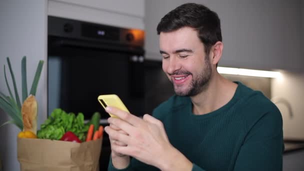 zbliżenie wideo przystojny młody mężczyzna za pomocą smartfona w domu kuchnia - Materiał filmowy, wideo