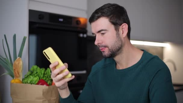primer plano de material de archivo de joven guapo utilizando el teléfono inteligente en la cocina casera - Metraje, vídeo