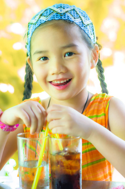 Asiatisches Mädchen trägt orangefarbenes Kleid mit Softdrink-Gläsern im Garten. - Foto, Bild