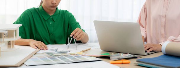 Ο σχεδιαστής εσωτερικών χώρων που χρησιμοποιεί αρχιτεκτονικό εξοπλισμό σχεδιάζει ένα σχέδιο, ενώ ο σχεδιαστής εσωτερικών χώρων επιλέγει το κατάλληλο χρώμα προσεκτικά χρησιμοποιώντας το laptop. Δημιουργικός σχεδιασμός και ομαδική εργασία. Ποικιλία. - Φωτογραφία, εικόνα