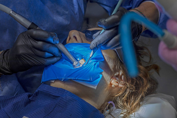 οδοντίατρος με μαύρα γάντια αντιμετωπίζει τα άρρωστα δόντια ενός ασθενούς - Φωτογραφία, εικόνα