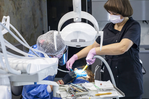 стоматолог і помічник в рукавичках лікують болісні зуби підлітка. Стоматологічна допомога та здоров'я - Фото, зображення