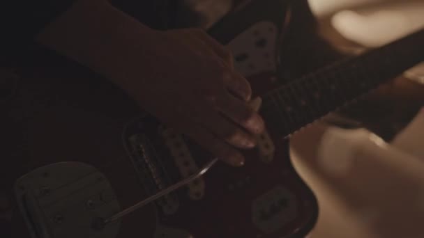 Colpo ritagliato di musicista maschile irriconoscibile che suona la chitarra elettrica nella stanza buia con raggi di luce gialla del proiettore su di lui - Filmati, video
