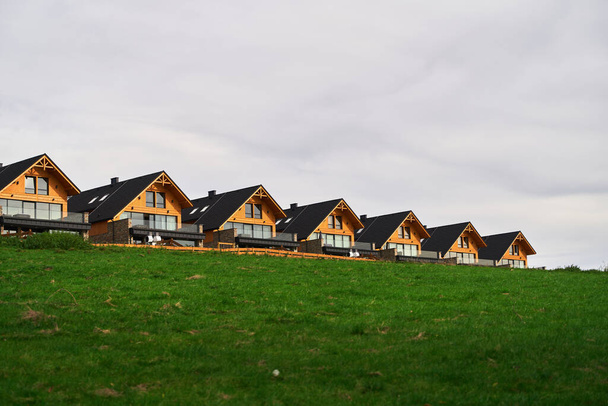 Une rangée de maisons modernes en bois nichées sur une colline verdoyante sous un ciel nuageux offrant un mélange de nature et d'architecture. - Photo, image