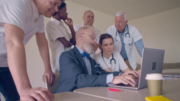 grupo de investigadores médicos en una sala de reuniones, reunidos alrededor de una computadora portátil para discutir su proyecto - Metraje, vídeo
