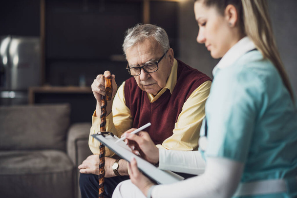 De huisarts is op bezoek bij een oudere man om zijn gezondheid te controleren. Professionele verzorger assisteert oude man in zijn huis. - Foto, afbeelding