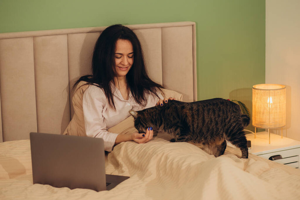 Studing en casa en línea. Mujer bastante joven usando el ordenador portátil mientras está sentado en la cama por la noche. Foto de alta calidad - Foto, imagen