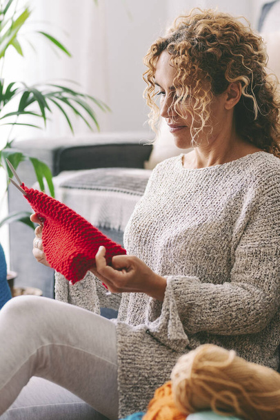 Vrouw zitten op de vloer Haakvideo een bal van rode wol. Handgemaakte creatie ontspannen op een zondagmiddag. Levensstijl en vrijetijdsbesteding - Foto, afbeelding