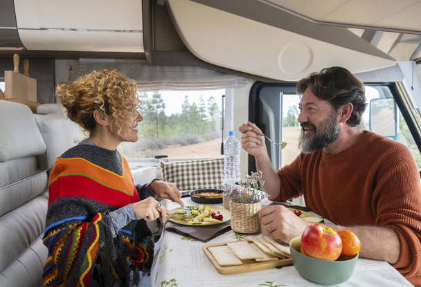 Пара путешественников, сидящих за столом в кемпере, обедают и отдыхают. Бородатый мужчина и блондинка разговаривают за обедом. Концепция путешествия и остановки для еды и отдыха - Фото, изображение