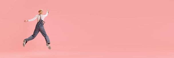 Banner. Vista trasera de la mujer joven en el aire. Chica en overoles de mezclilla saltando a pintar graffiti sobre fondo rosa con espacio negativo para insertar texto. Concepto de juventud, moda, urbano, cultura. - Foto, Imagen