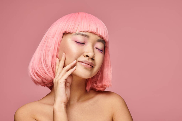 asian woman with pink hair and closed eyes touching her cheek on vibrant background - Photo, image