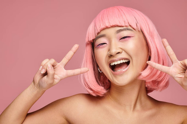 attractive asian woman with nose piercing showing peace sign and smiling on vibrant background - Foto, immagini