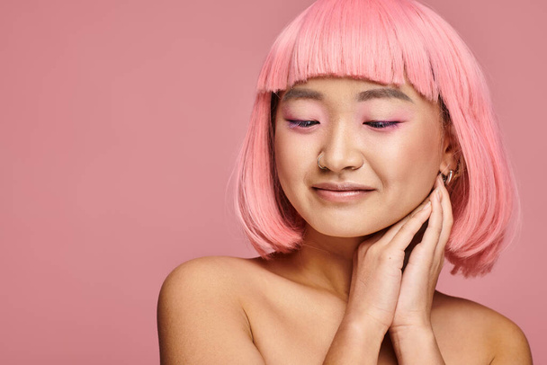 pretty asian woman with pink hair and makeup looking to down with hands on vibrant background - Φωτογραφία, εικόνα