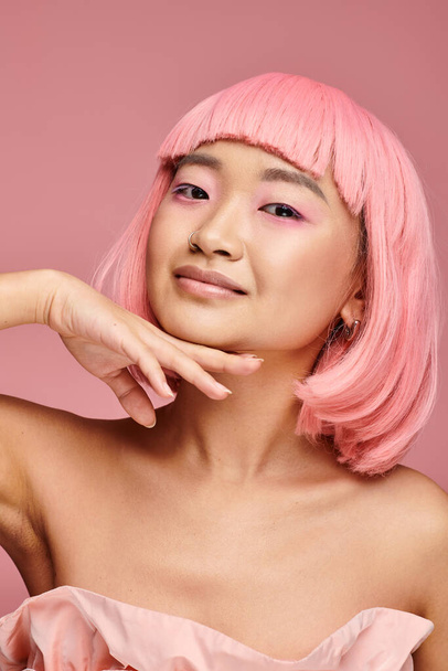 alluring asian woman in 20s with pink hair touching to chin with hand on vibrant background - Valokuva, kuva
