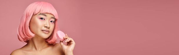 horizontal shot of asian young woman with pink hair posing with macaroon on vibrant background - Photo, Image