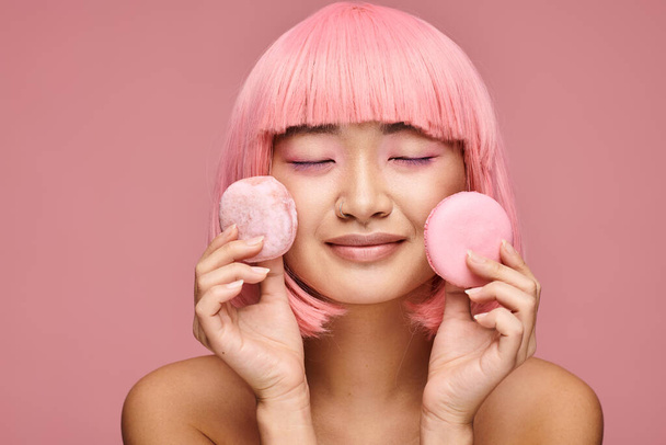 happy asian woman with pink hair and closed eyes posing with sweets in vibrant background - Photo, Image