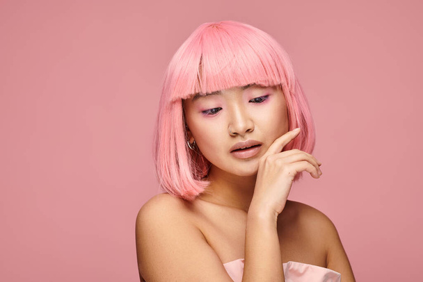 alluring asian young woman with pink hair touching to chin and looking to down in vibrant background - Photo, Image