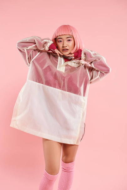 pretty asian young woman with pink hair and makeup posing with hands on head on vibrant background - Foto, afbeelding