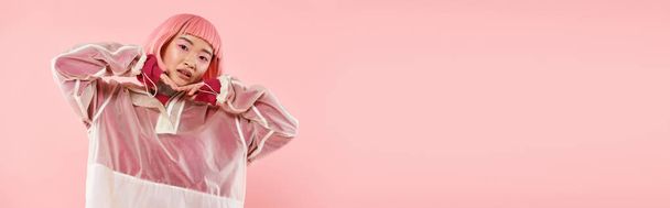 horizontal shot of asian young woman with pink hair posing with hands on head on vibrant background - Photo, Image