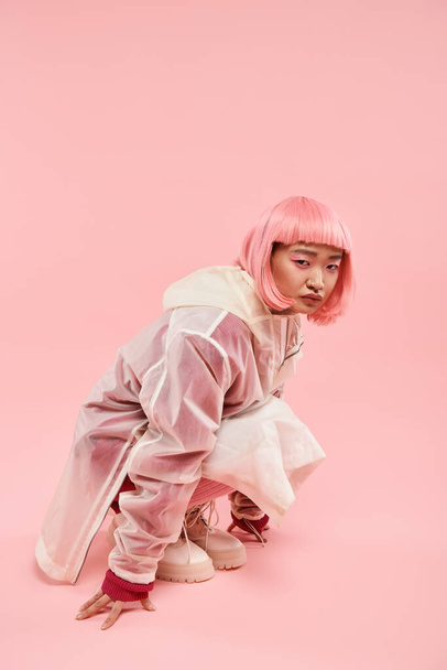 słodkie Azji kobieta w 20s z różowe włosy w stylowy strój przykucnął w dół na żywe tło - Zdjęcie, obraz