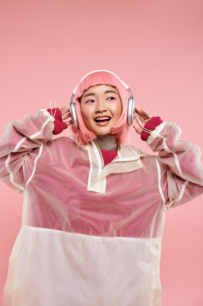 cute asian young girl with pink hair listening to music with headphones against vibrant background - Photo, Image