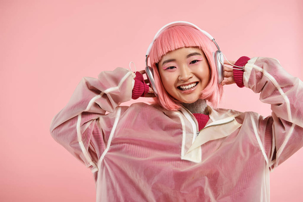 beautiful asian girl in 20s  with pink hair listening to music with headphones on vibrant background - Фото, изображение