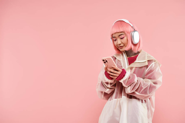 lovely asian woman with pink hair in headphones texting in smartphone on vibrant background - Photo, Image