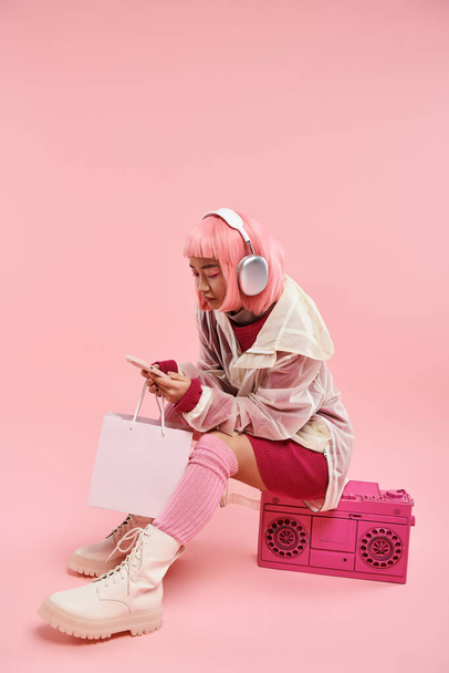 attractive asian young in headphones texting in smartphone and sittings on boombox - Photo, Image