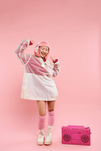 jovem alegre com cabelo rosa em fones de ouvido dançando com música em fundo vibrante - Foto, Imagem
