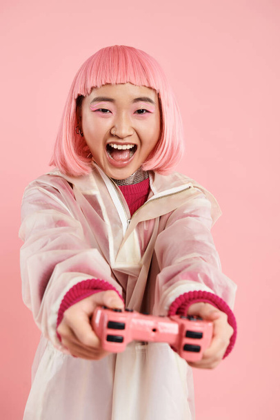 mooie aziatische vrouw in 20s in stijlvolle outfit gelukkig spelen naar joystick tegen levendige achtergrond - Foto, afbeelding