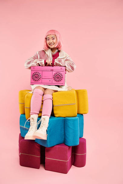 hermosa mujer asiática con pelo rosa sentado en grandes puzzles con boombox sobre fondo vibrante - Foto, imagen
