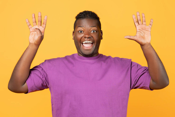 Excited African American man raising both hands showing number nine, open palms with five and four fingers over yellow studio background, counting to nine, smiling to camera - Photo, Image