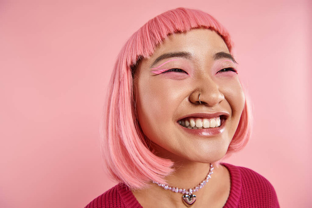 primer plano de asiático joven mujer con nariz piercing feliz riendo en rosa fondo - Foto, imagen