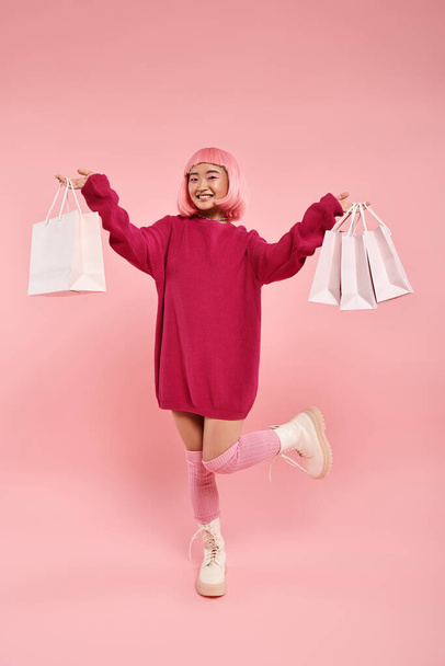 słodkie Azji kobieta w jej 20s pozowanie z nogi podniesiony i trzymając zakupy torby na różowym tle - Zdjęcie, obraz
