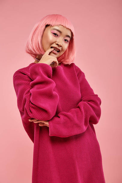 pretty young woman with pink hair posing and biting nail against vibrant background - Foto, Bild