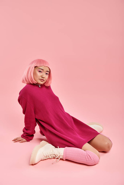 ελκυστική γυναίκα 20 ετών με ροζ μαλλιά σε μεγάλο πουλόβερ στολή χαλαρή κάθεται σε ζωντανό φόντο - Φωτογραφία, εικόνα