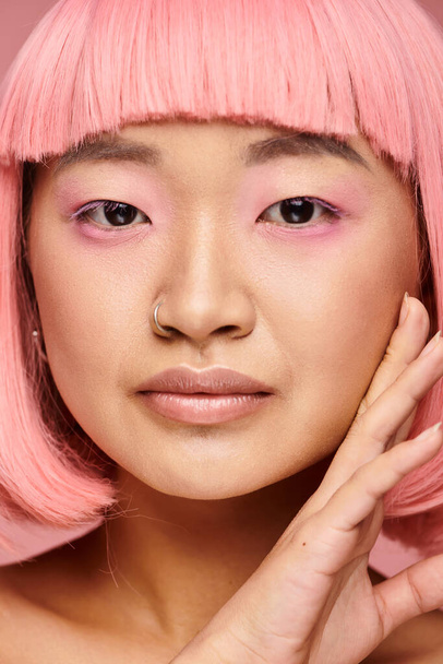Крупный план красивой азиатской женщины в возрасте 20 лет с пирсингом носа касательно лица на ярком фоне - Фото, изображение