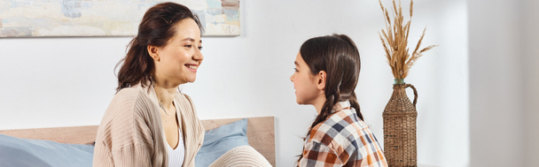Μια μητέρα και η κόρη έχουν μια εγκάρδια συζήτηση σε ένα ζεστό και φιλόξενο υπνοδωμάτιο. - Φωτογραφία, εικόνα
